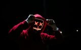 A spooky illuminated mask figure with a red hoodie in a dark setting, perfect for Halloween themes.